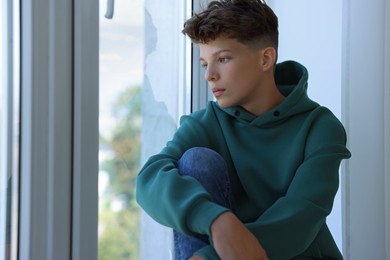 Loneliness concept. Sad teenage boy near window indoors