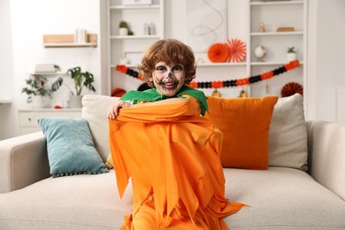 Funny boy dressed like pumpkin for Halloween celebration in room