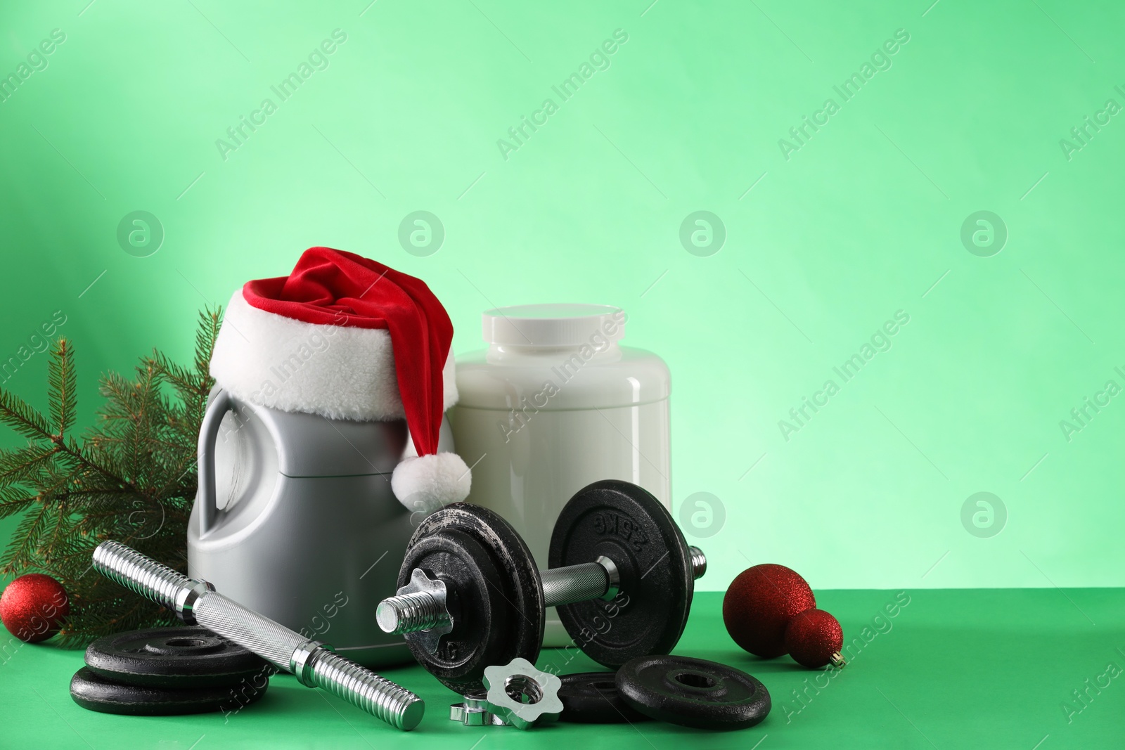 Photo of Dumbbells, containers with supplements and Christmas decor on green background. Space for text