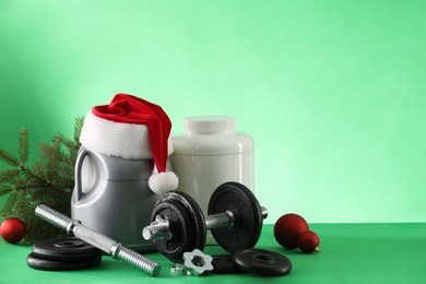 Photo of Dumbbells, containers with supplements and Christmas decor on green background. Space for text