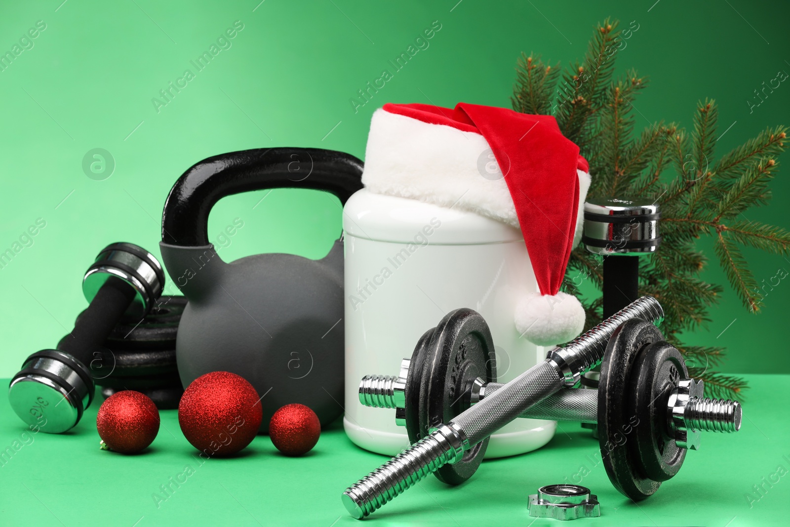 Photo of Dumbbells, kettlebell, container with supplement and Christmas decor on green background