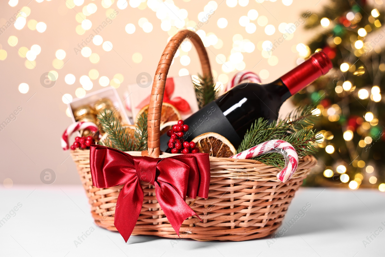 Photo of Wicker gift basket with wine and Christmas decor on light table