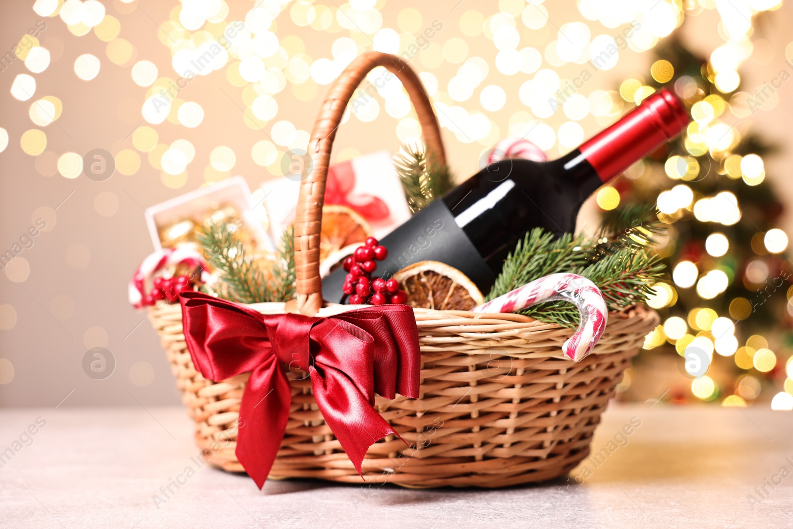 Photo of Wicker gift basket with wine and Christmas decor on light textured table