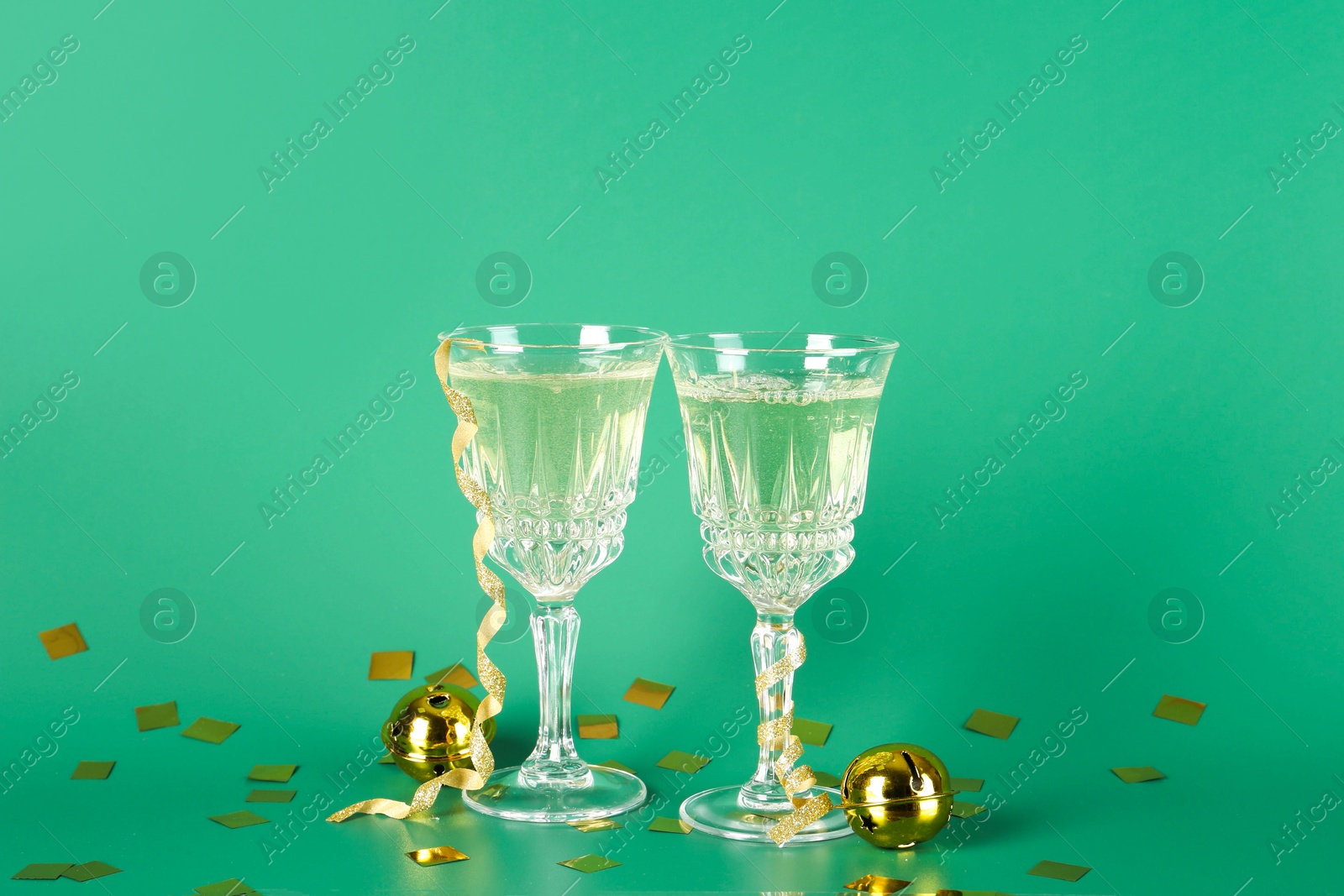 Photo of Sparkling wine in glasses, confetti and other Christmas decor on green background