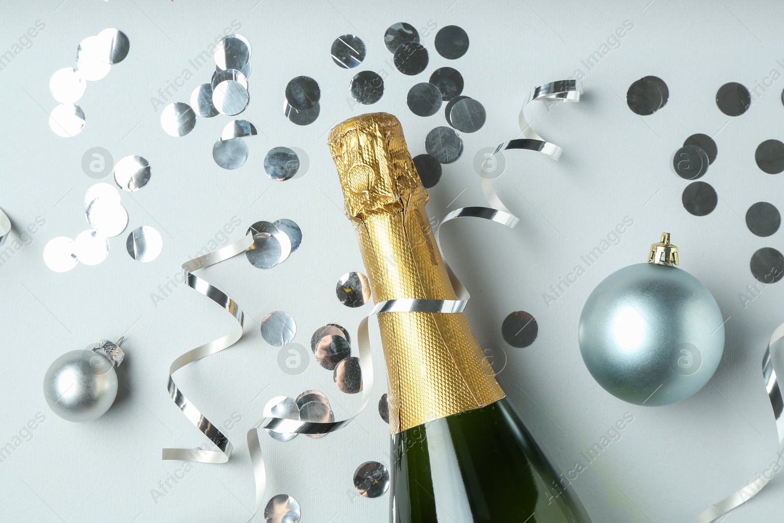 Photo of Flat lay composition with bottle of sparkling wine, shiny confetti and other Christmas decor on light grey background