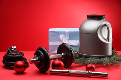 Photo of Dumbbells, container with supplement and Christmas decor on red background. Space for text