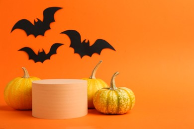 Photo of Halloween celebration. Black paper bats, pumpkins and podium on orange background, space for text