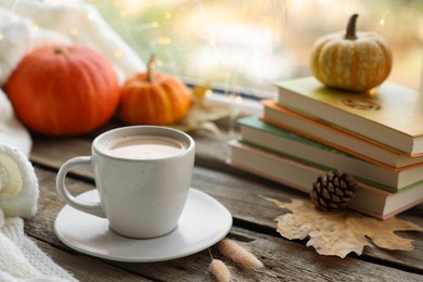 Cup of coffee, books and autumn decor on wooden table, closeup