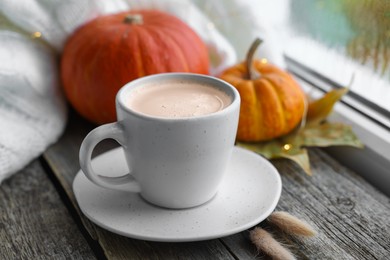 Photo of Cup of coffee and autumn decor on window sill, closeup