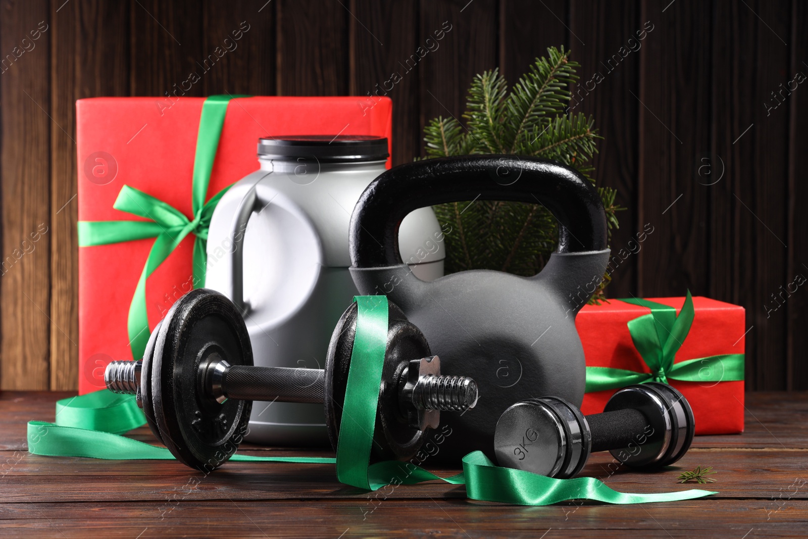 Photo of Dumbbells, container with supplement, kettlebell and Christmas decor on wooden table