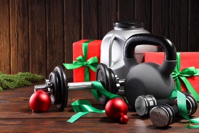 Photo of Dumbbells, container with supplement, kettlebell and Christmas decor on wooden table