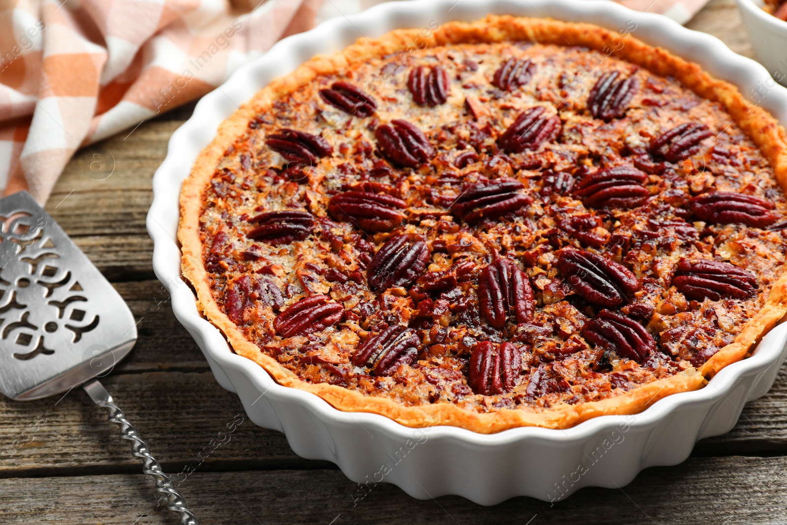 Photo of Delicious pecan pie in baking dish and cake server on wooden table, closeup