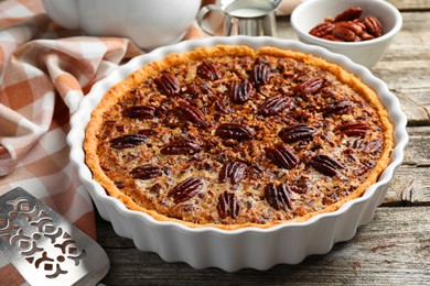 Photo of Delicious pecan pie in baking dish and cake server on wooden table, closeup