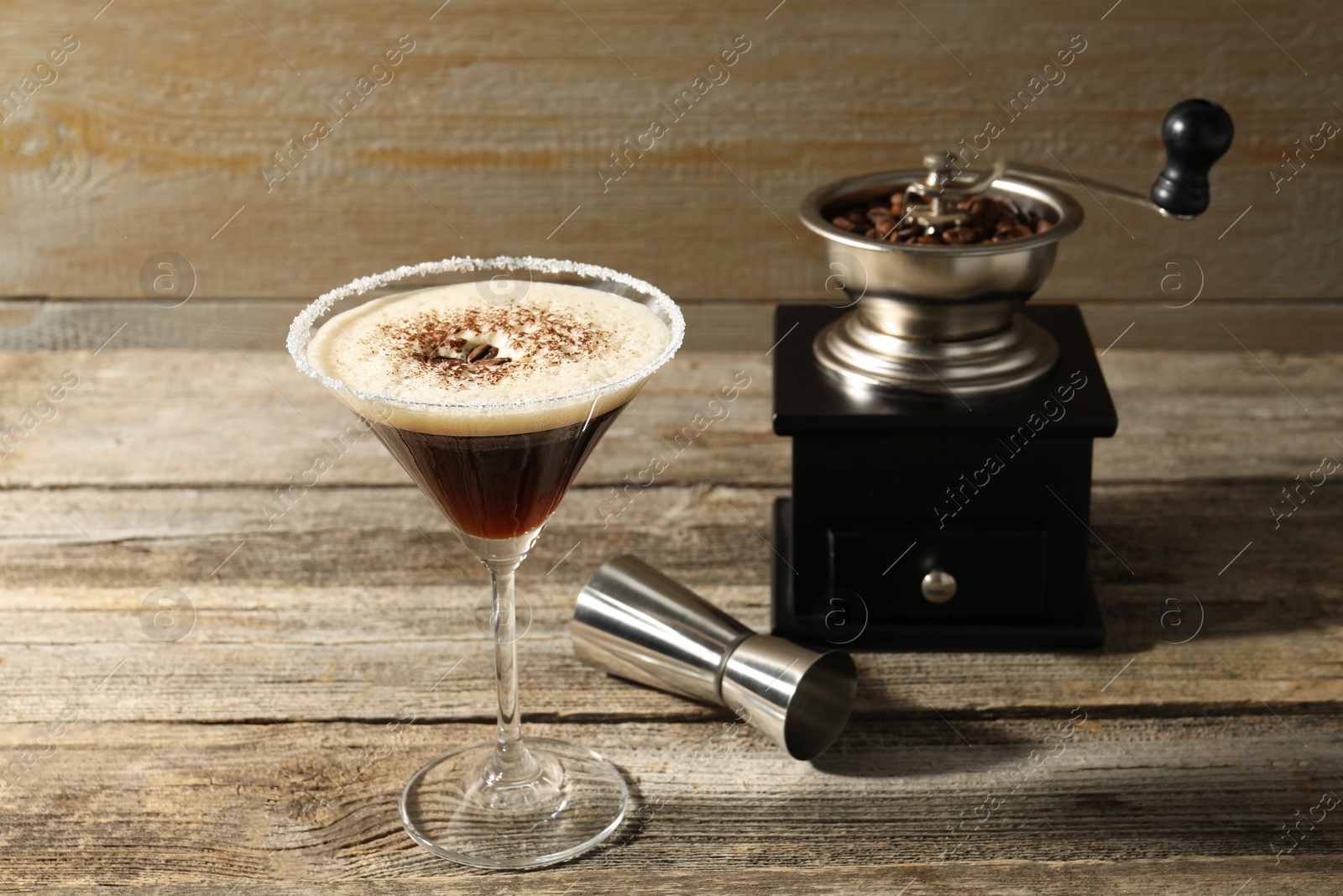 Photo of Glass of fresh cocktail, manual coffee grinder and jigger on wooden table