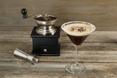 Glass of fresh cocktail, manual coffee grinder and jigger on wooden table