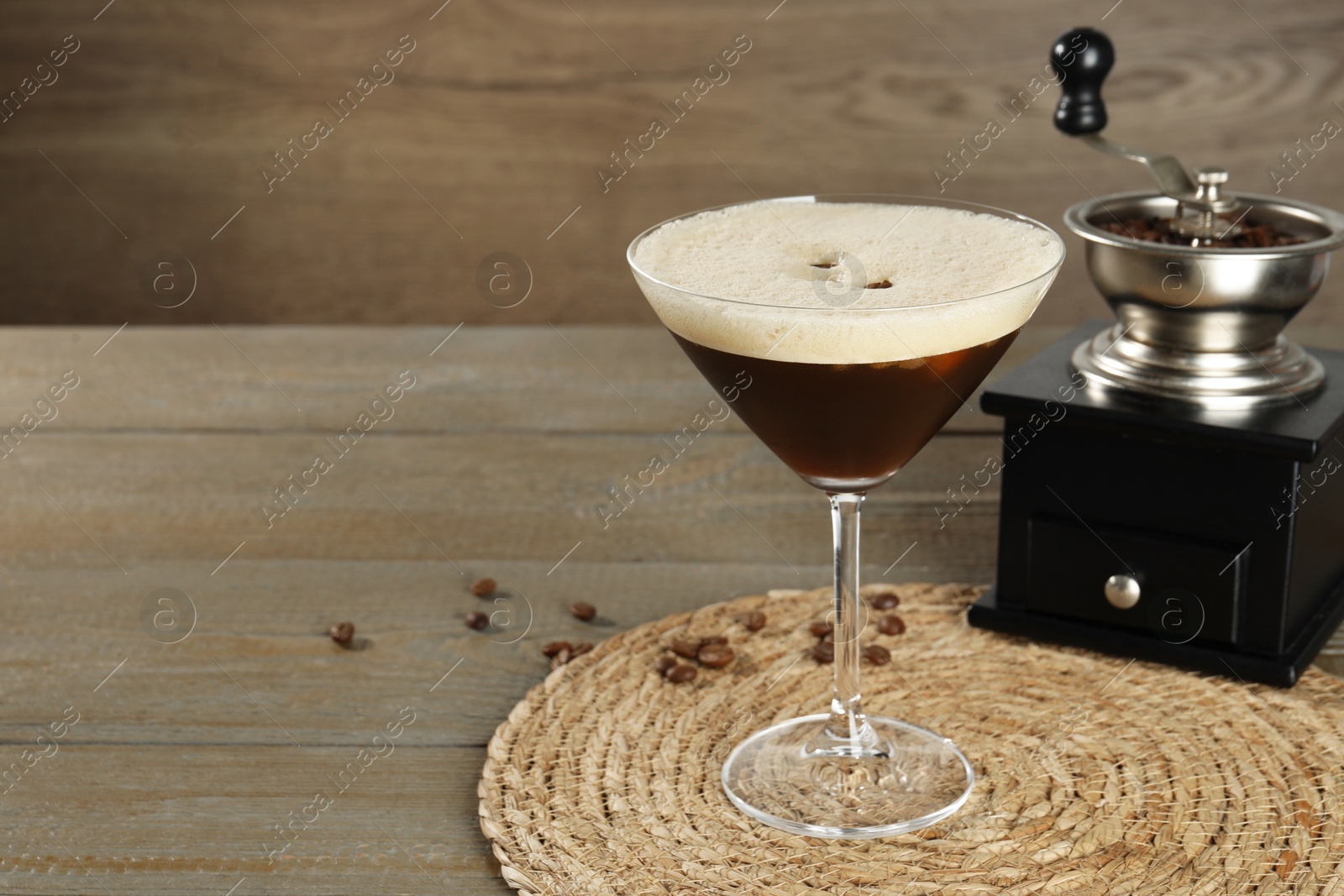 Photo of Glass of fresh cocktail and manual coffee grinder on wooden table, space for text