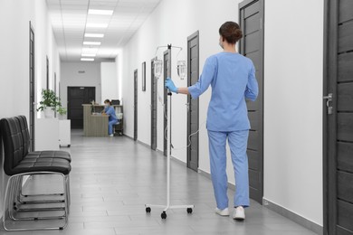 Nurse with IV drip in hospital hallway, back view