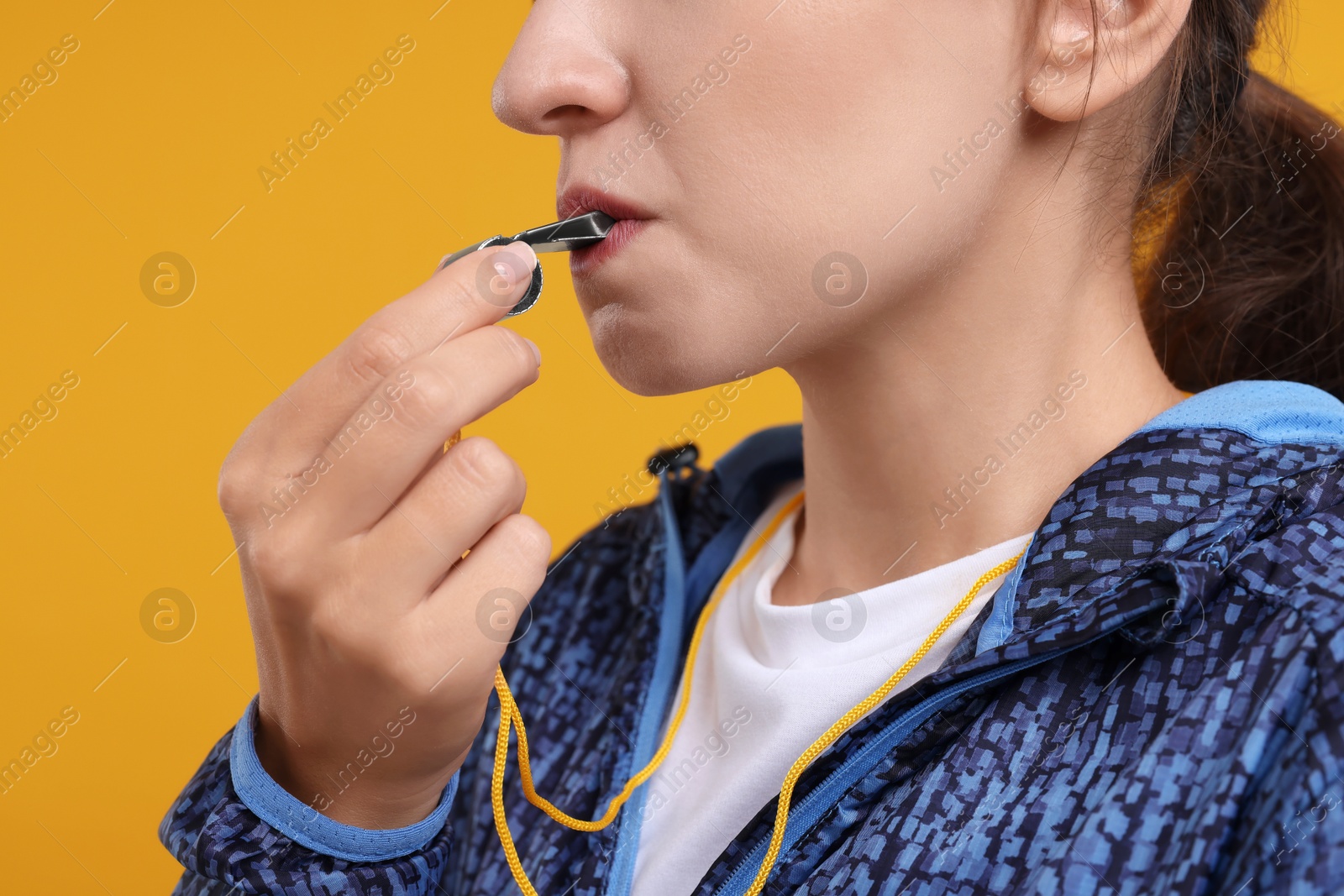 Photo of Woman blowing whistle on orange background, closeup