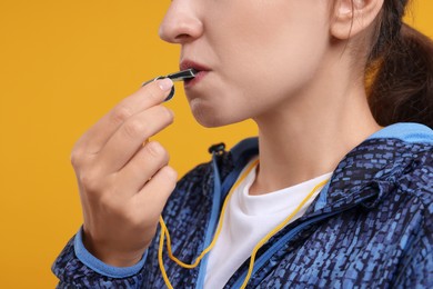 Woman blowing whistle on orange background, closeup