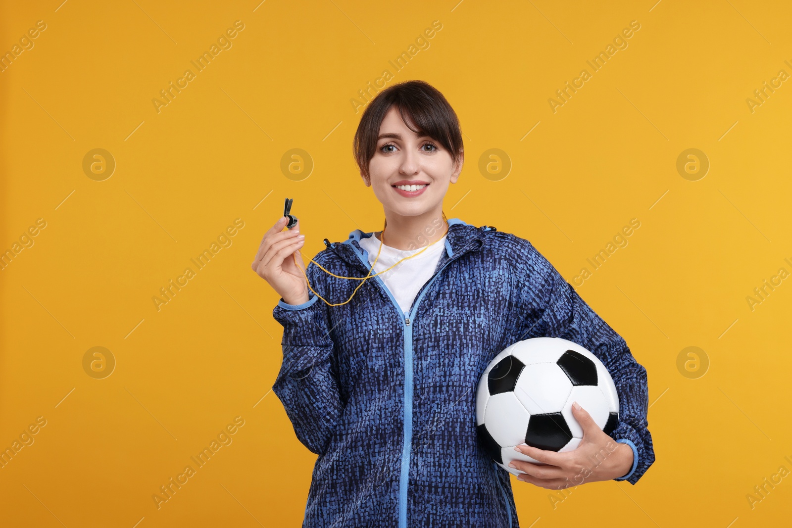 Photo of Happy woman with whistle and soccer ball on orange background