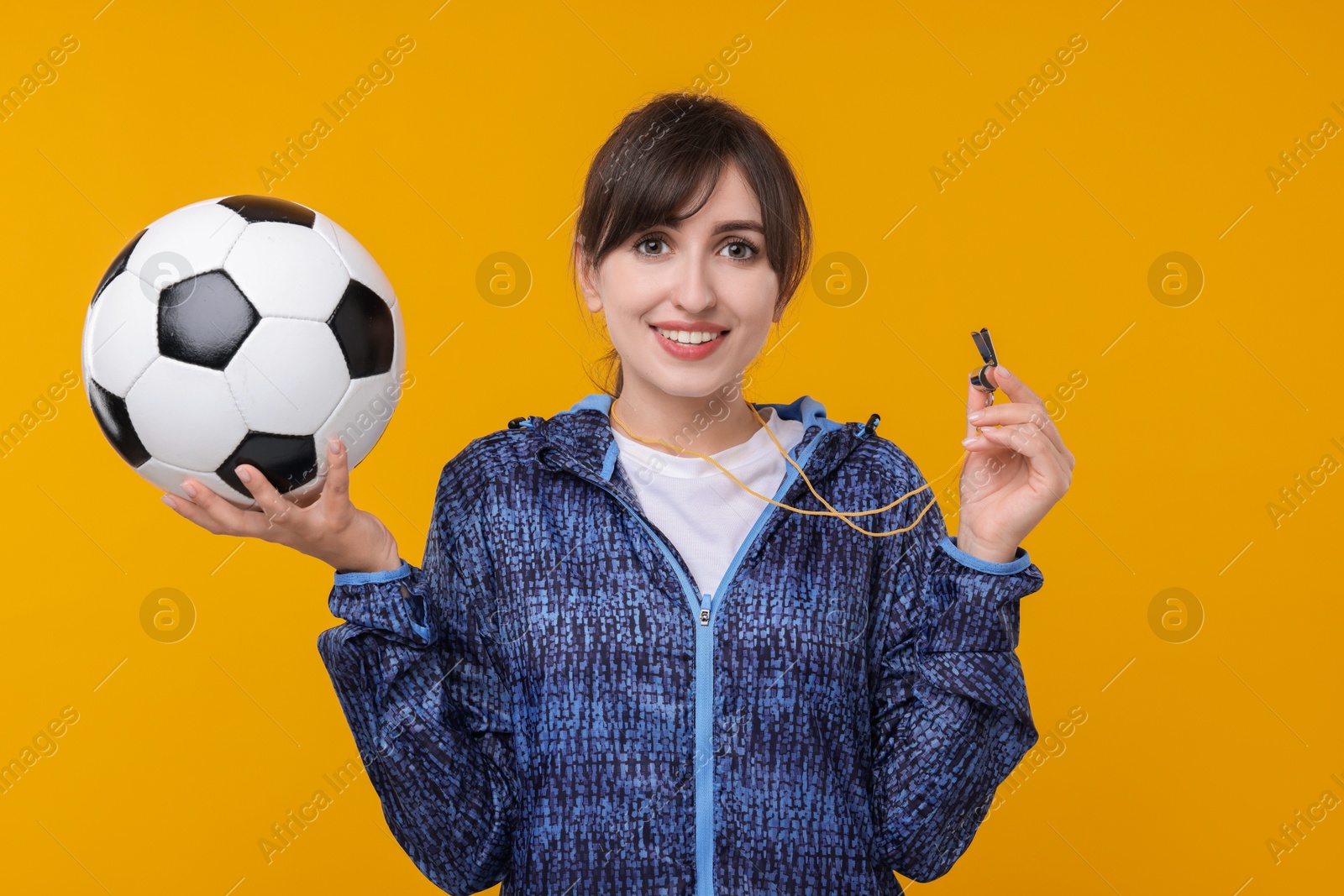 Photo of Happy woman with whistle and soccer ball on orange background