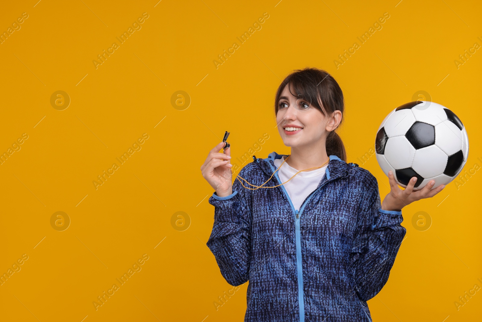 Photo of Happy woman with whistle and soccer ball on orange background, space for text