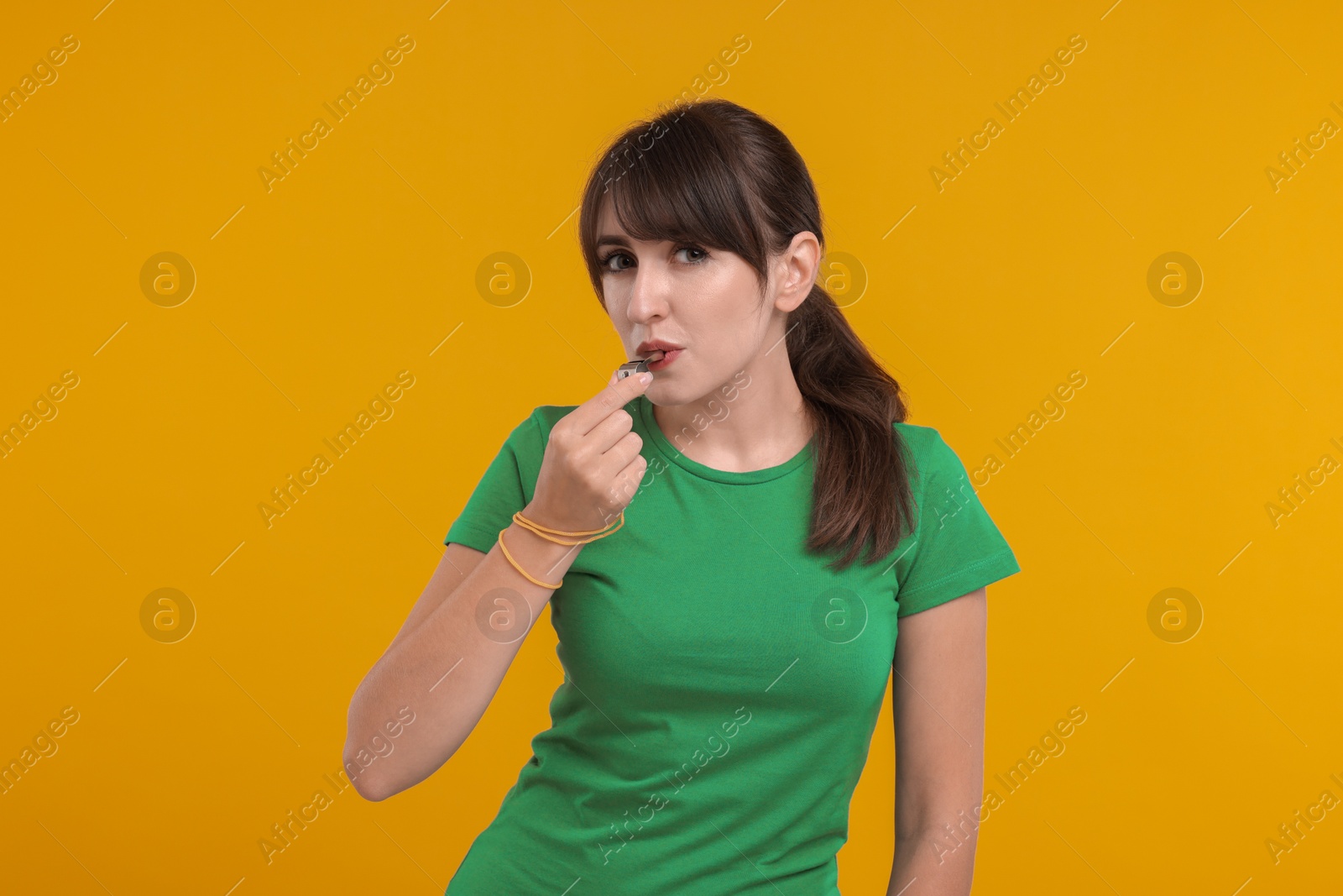 Photo of Young woman blowing whistle on orange background