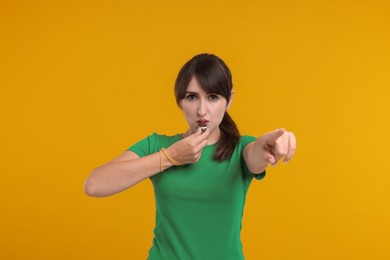 Photo of Young woman blowing whistle on orange background