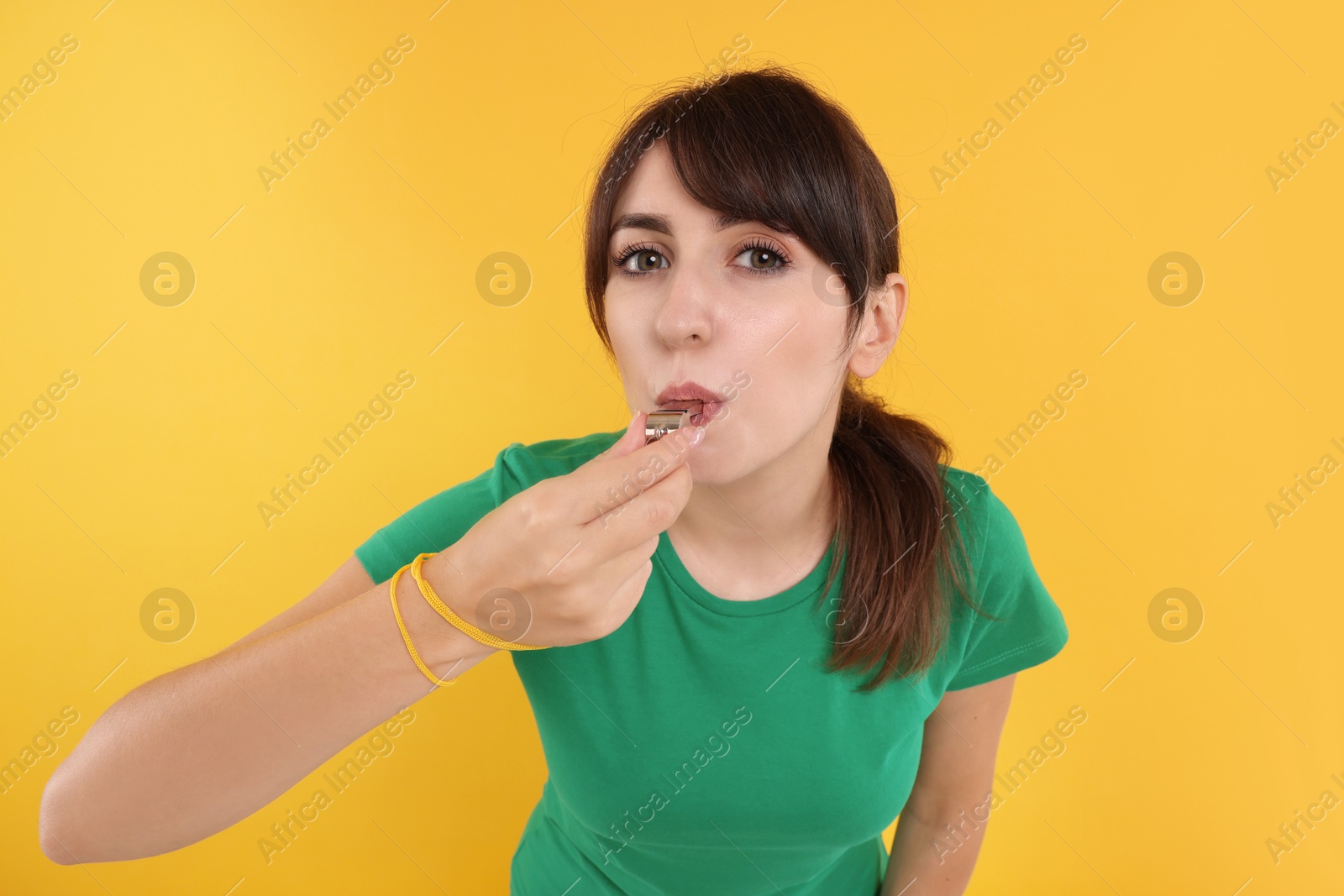 Photo of Young woman blowing whistle on orange background