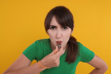 Photo of Young woman blowing whistle on orange background