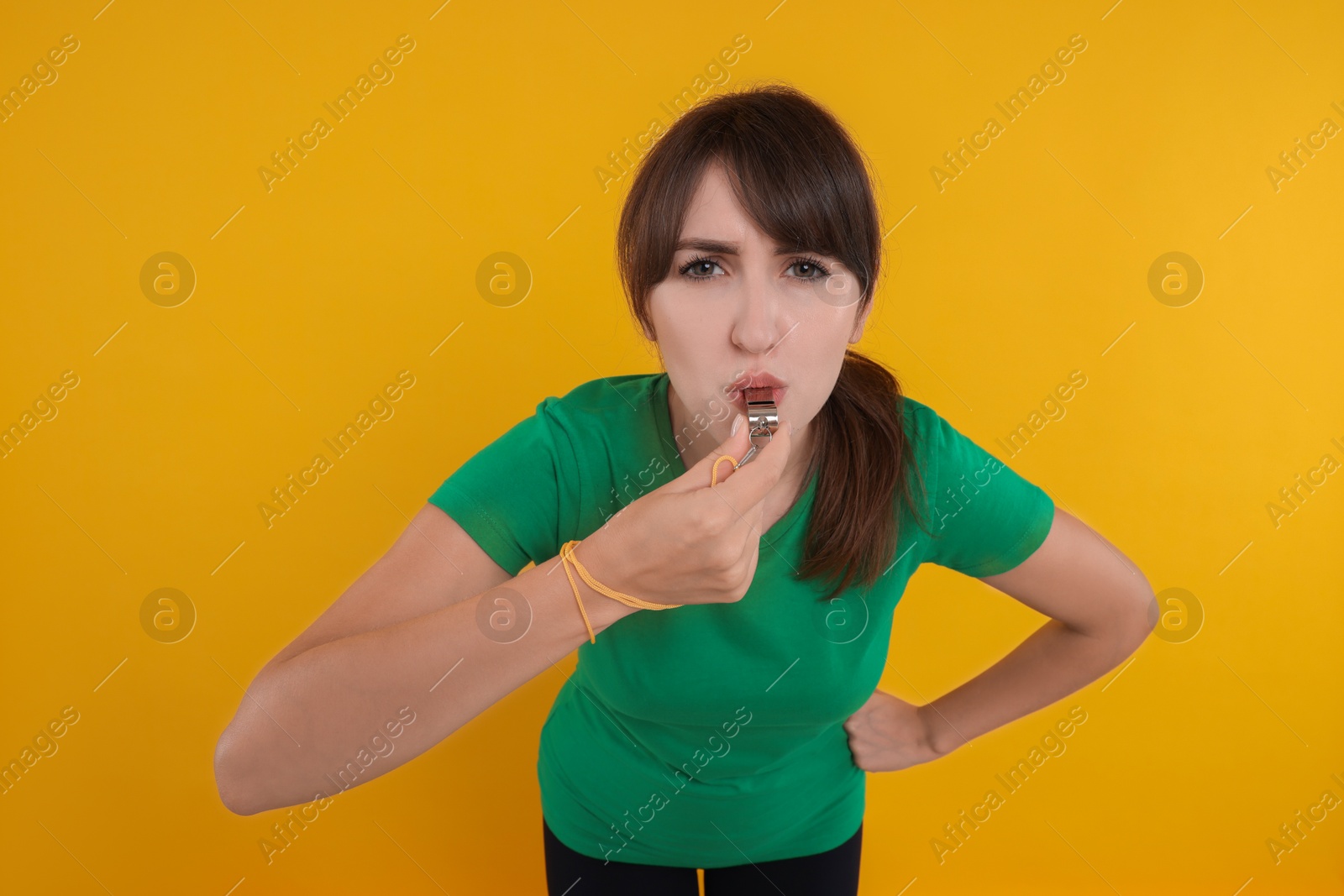 Photo of Young woman blowing whistle on orange background