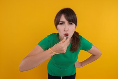 Young woman blowing whistle on orange background