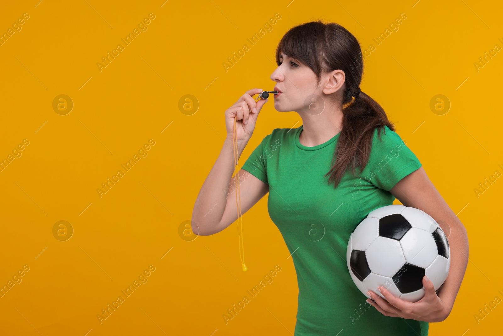 Photo of Woman with soccer ball blowing whistle on orange background, space for text