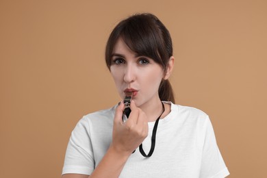 Young woman blowing whistle on beige background