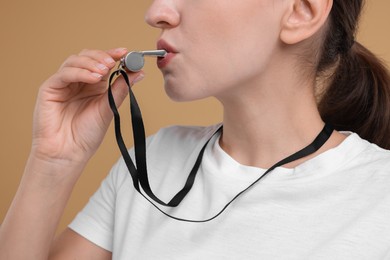 Woman blowing whistle on beige background, closeup