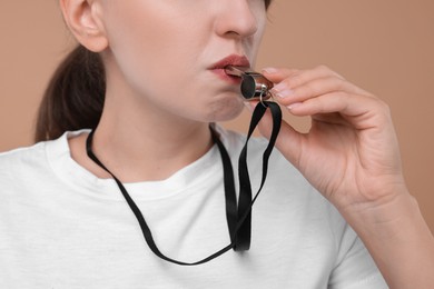 Photo of Woman blowing whistle on beige background, closeup