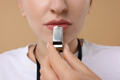 Woman with whistle on beige background, closeup