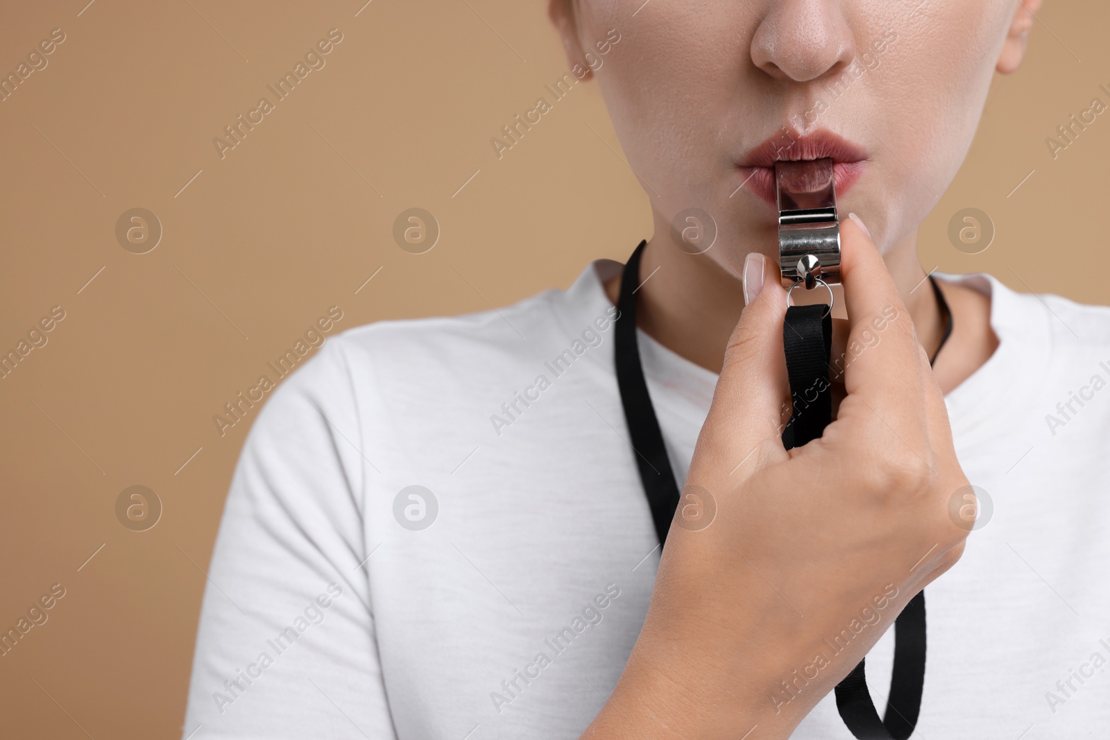 Photo of Woman blowing whistle on beige background, closeup