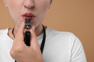 Woman blowing whistle on beige background, closeup