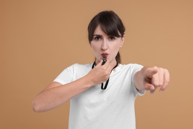 Photo of Young woman blowing whistle on beige background