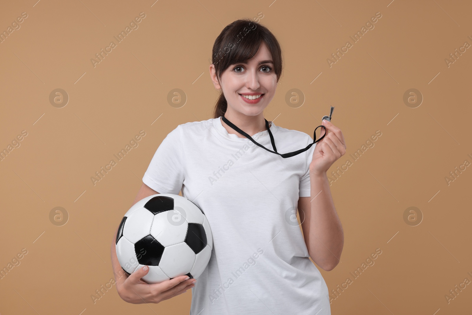 Photo of Happy woman with whistle and soccer ball on beige background