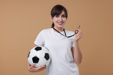 Happy woman with whistle and soccer ball on beige background