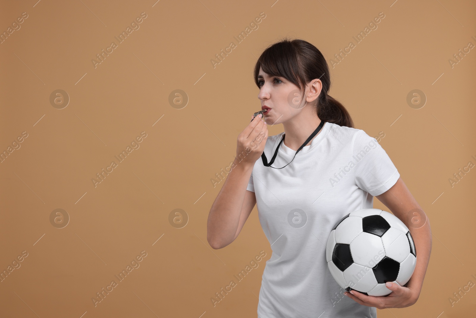 Photo of Woman with soccer ball blowing whistle on beige background, space for text