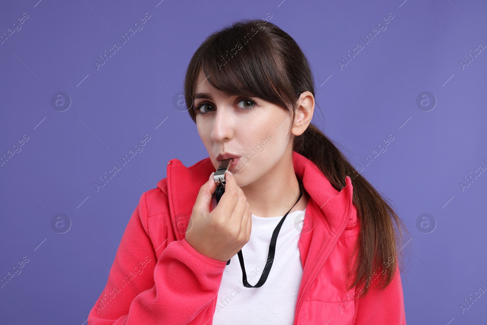 Photo of Young woman blowing whistle on purple background