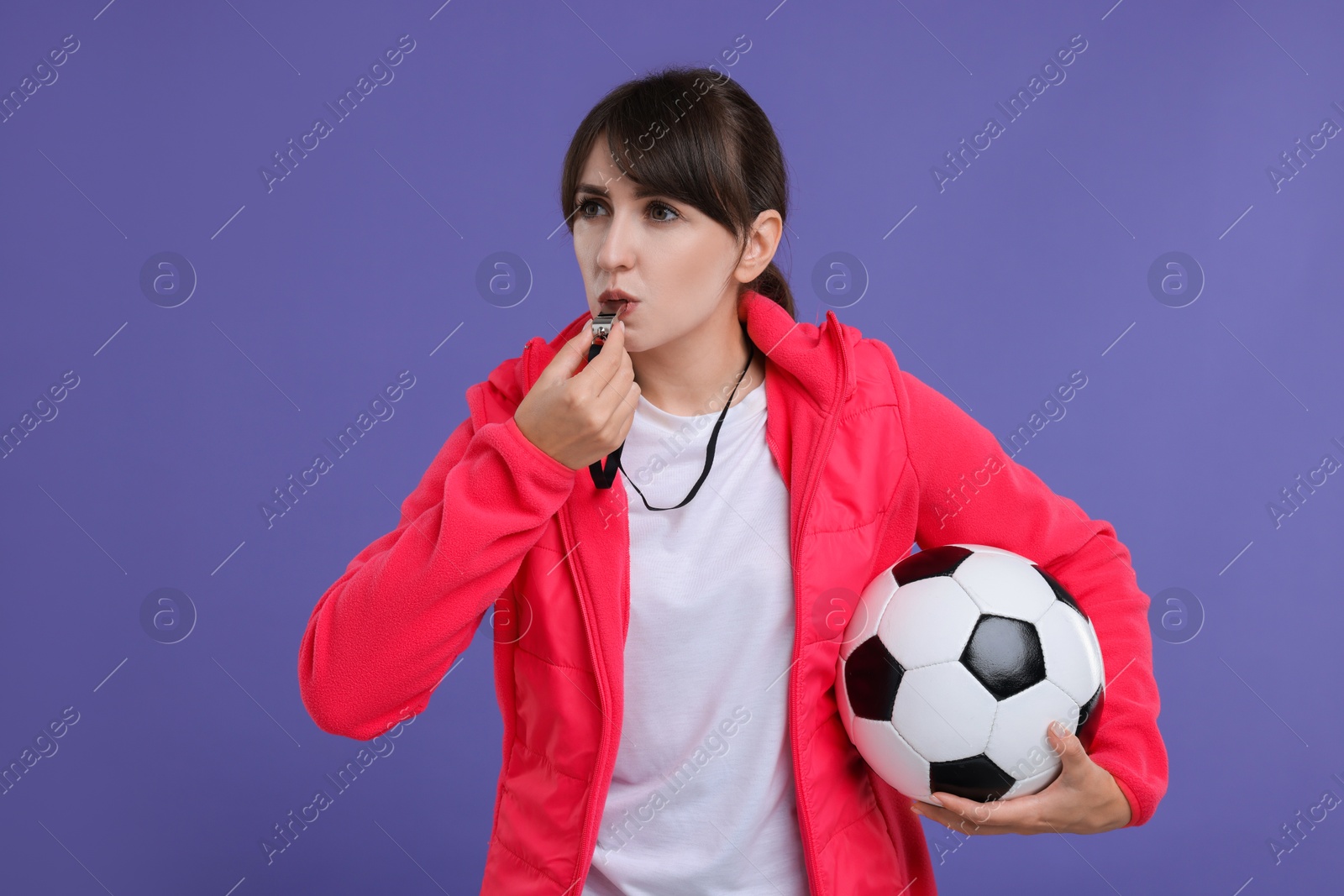 Photo of Woman with soccer ball blowing whistle on purple background