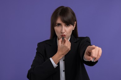 Young woman blowing whistle on purple background