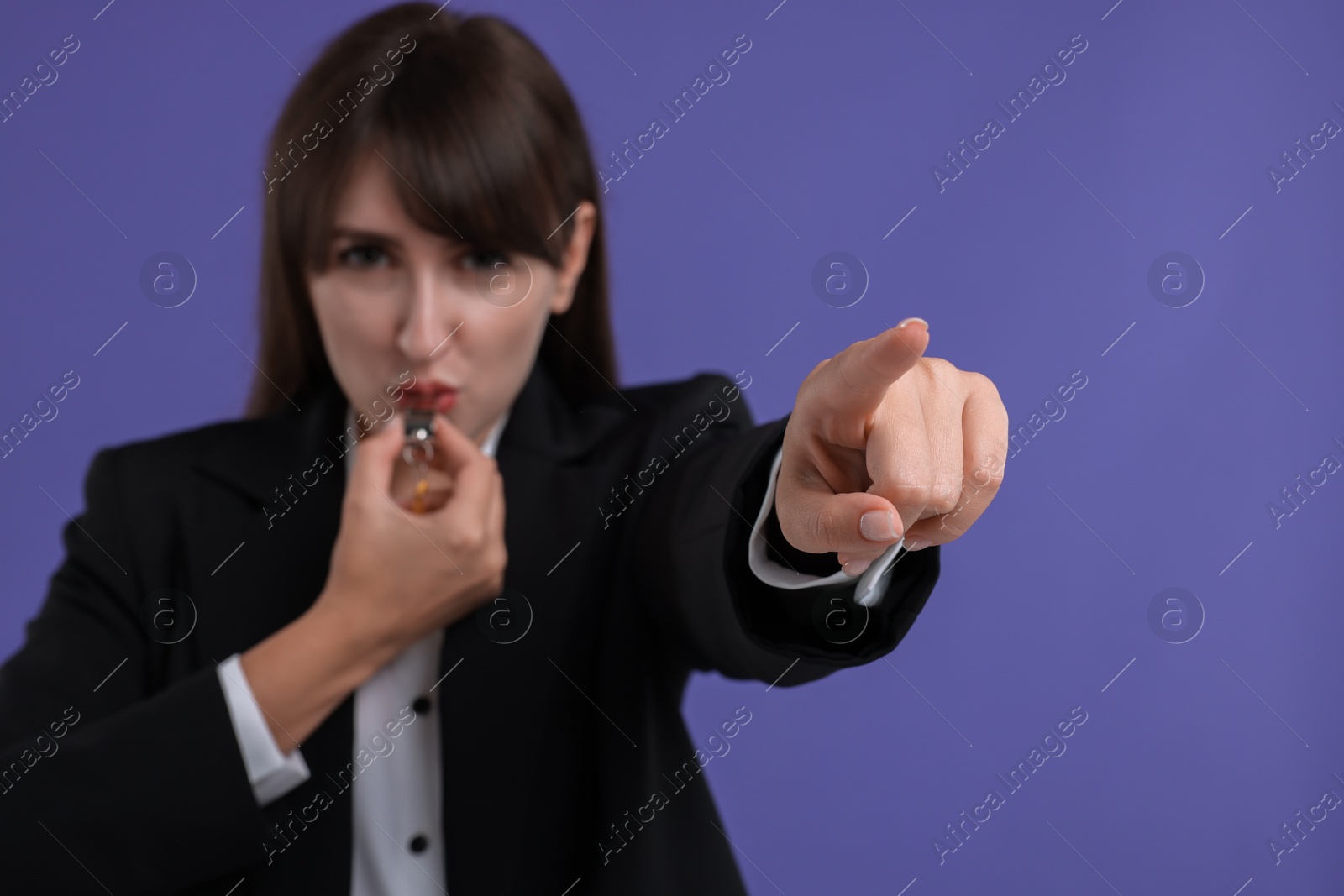 Photo of Woman blowing whistle on purple background, selective focus