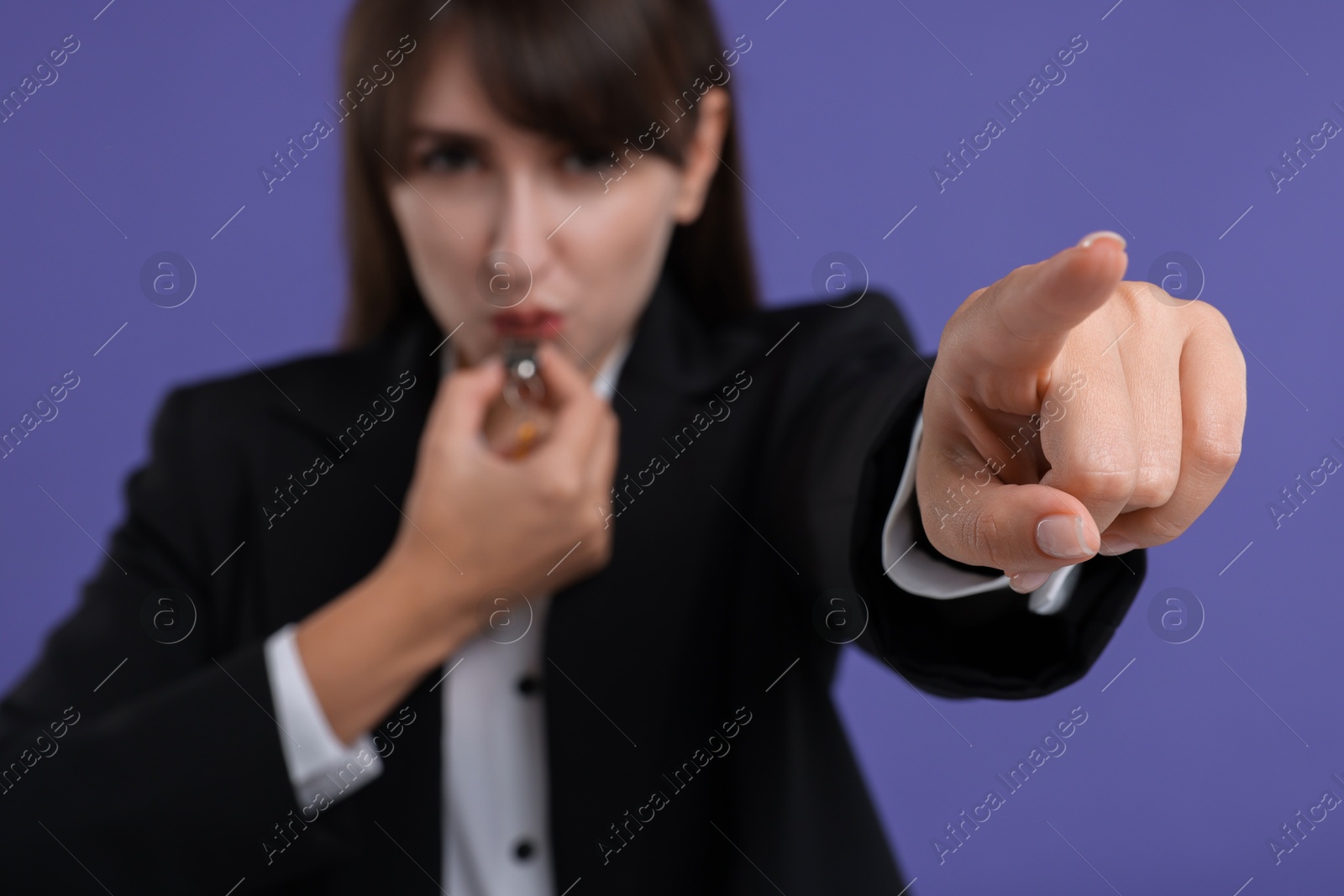 Photo of Woman blowing whistle on purple background, selective focus