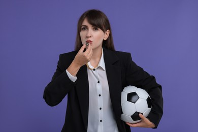 Woman with soccer ball blowing whistle on purple background