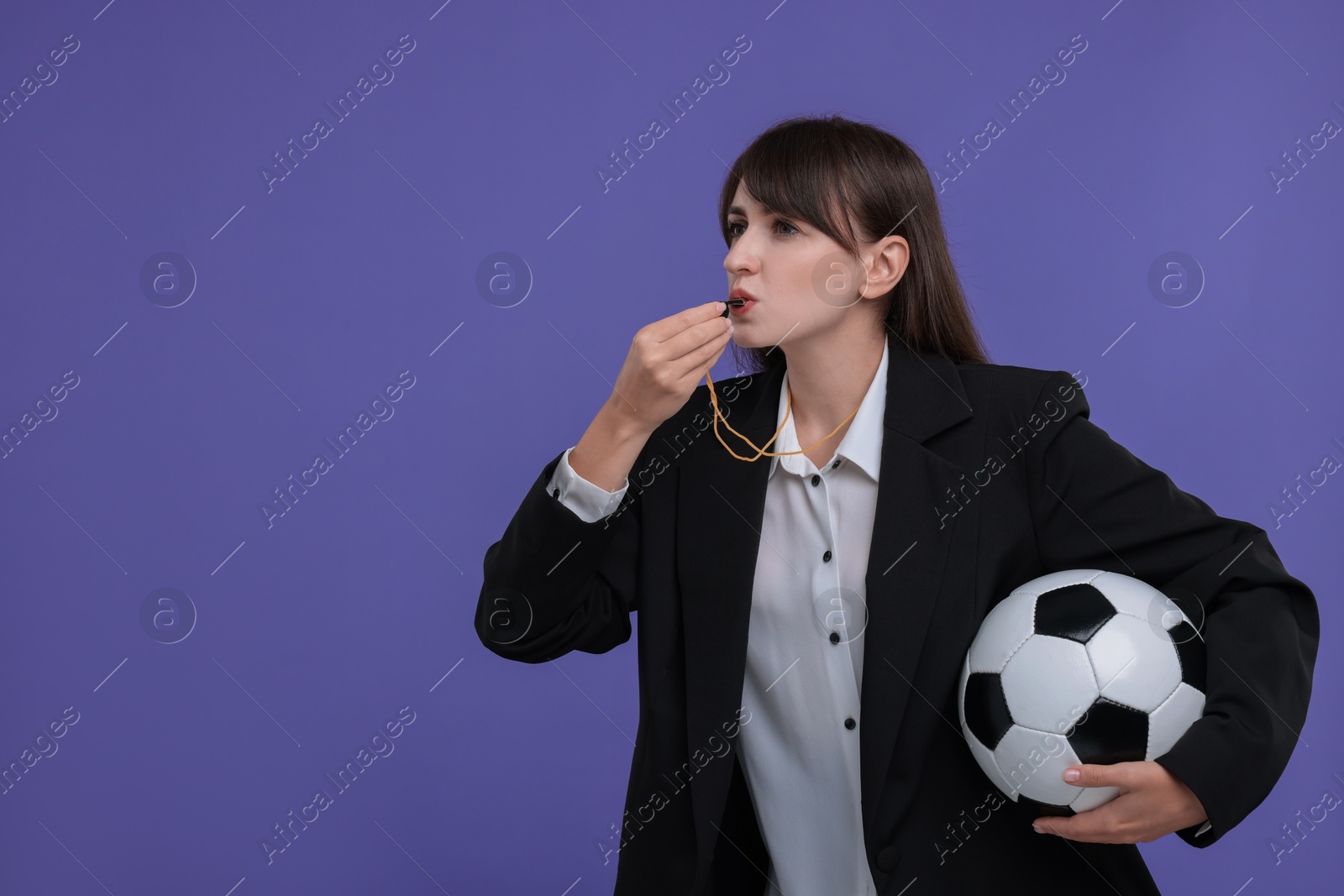 Photo of Woman with soccer ball blowing whistle on purple background, space for text